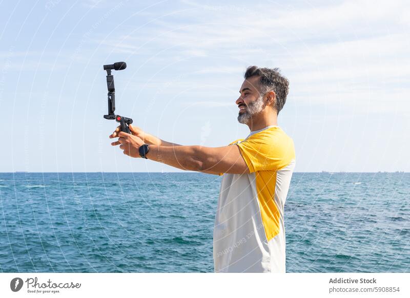 Mann nimmt Video mit Gimbal am Meer auf Inder Sport Sommer Seeküste Aufnahme Kardangelenk Technik & Technologie Gerät Apparatur Wasser MEER Blauer Himmel