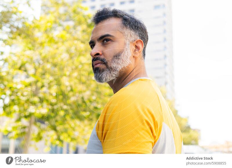 Indischer Mann in Sportkleidung, der in einer sommerlichen Umgebung wegschaut Inder Sportbekleidung Sommer urban Park Wegsehen nachdenklich Stehen im Freien