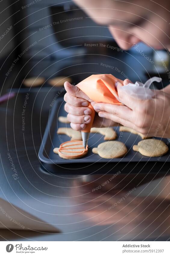 Dekorieren von selbstgebackenen Halloween-Keksen auf einer Küchentheke Dekoration & Verzierung selbstgemacht Arbeitsplatte Zuckerguß orange Person Hand