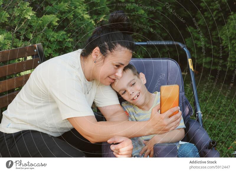 Mutter und Sohn genießen die Zeit im Freien, beide lächeln und beschäftigen sich zerebrale Kinderlähmung Rollstuhl Smartphone Lächeln Glück Familie Pflege