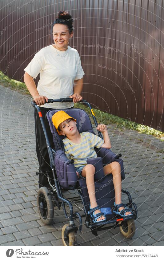 Mutter geht mit Sohn mit zerebraler Lähmung im Rollstuhl spazieren zerebrale Kinderlähmung Behinderung im Freien Pflege binden abstützen Mobilität