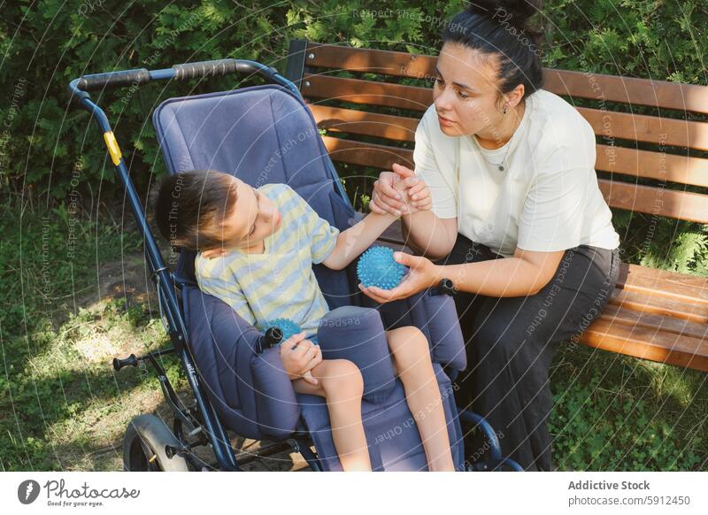 Mutter und Sohn mit zerebraler Lähmung genießen die Zeit im Freien zerebrale Kinderlähmung Rollstuhl Park Pflege Behinderung abstützen Liebe taktil Interaktion