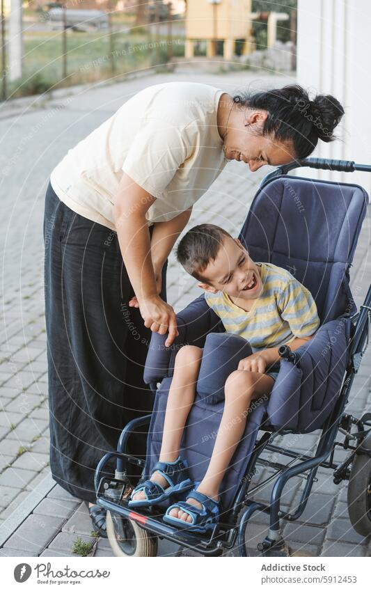 Mutter bindet sich an Sohn mit zerebraler Lähmung im Rollstuhl zerebrale Kinderlähmung Bonden im Freien Lächeln Pflege Liebe Behinderung Interaktion familiär