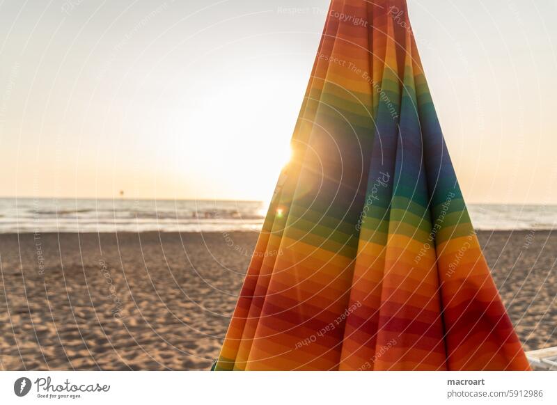 bunt gestreifter, geschlossener Sonnenschirm in Nahaufnahme am Strand bei Sonnenuntergang streifen sonnenschirm zu sand strand sandstrand meer wasser