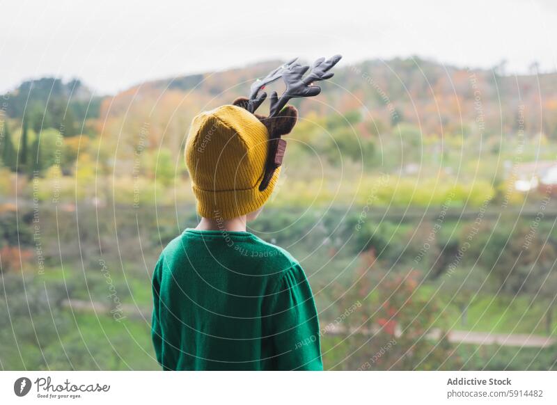 Kind mit Rentiergeweih mit Blick auf die Herbstlandschaft gelbe Mütze grüner Pullover Landschaft hohe Aussichtslage festlich Weihnachten im Freien malerisch