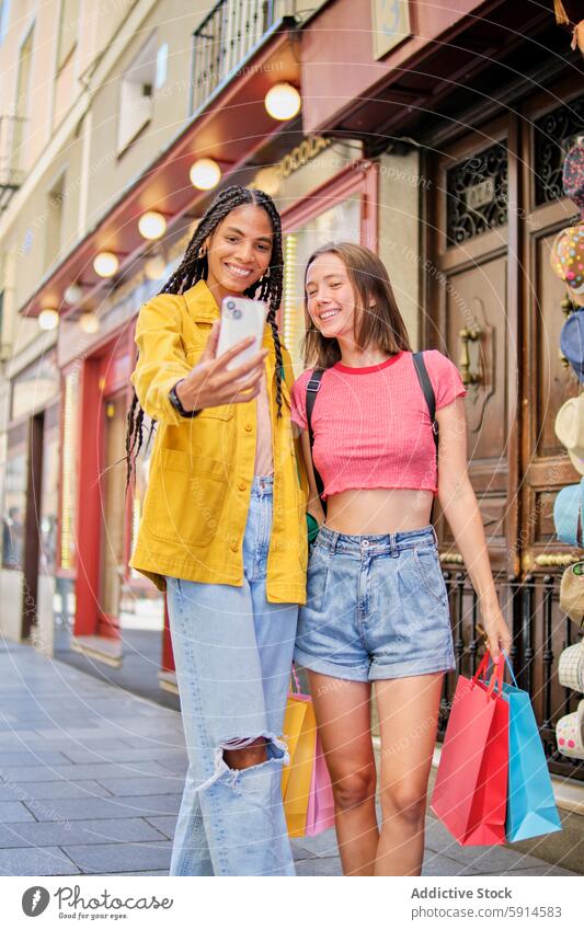 Zwei junge multiethnische Frauen genießen das Einkaufen und machen ein Selfie Smartphone Tasche heiter Lächeln Großstadt Straße Mode Jugend Freundschaft