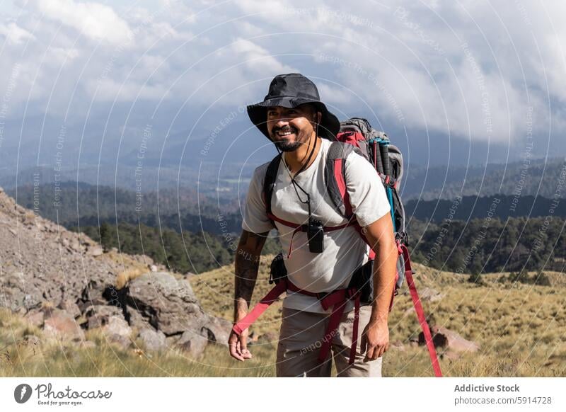 Männlicher Wanderer lächelt beim Trekking auf einem schlafenden Vulkan männlich Vollbart Tattoo Hut Rucksack Trekkingstock Lächeln Direkter Blick Fotokamera