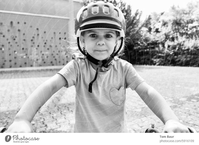 Ready to bike! - Mädchen mit Helm sitzt auf dem Fahrrad und schaut in die Kamera portät Fahrradhelm Kindheit 3-8 Jahre Bewegung Schwarzweißfoto Außenaufnahme