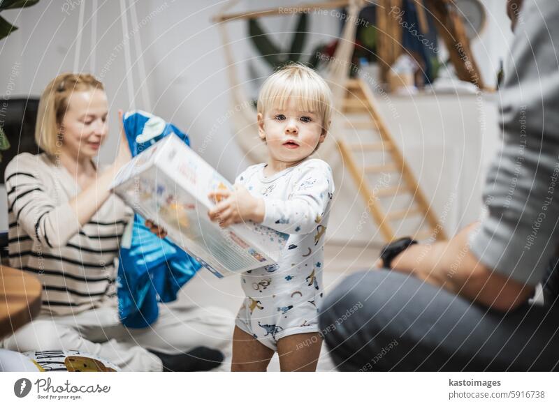 Niedliches kleines blondes kaukasisches Kleinkind packt Weihnachts- oder Geburtstagsgeschenk aus. Bezaubernder kleiner Säugling Baby Junge öffnet Geschenk Kind