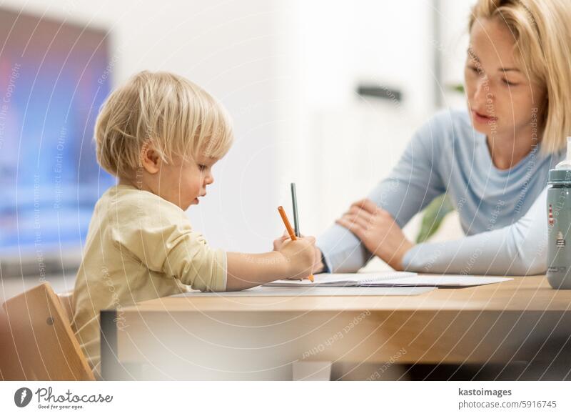 Caring junge kaukasische Mutter und kleinen Sohn Zeichnung Malerei in Notebook zu Hause zusammen. Liebevolle Mutter oder Kindermädchen mit Spaß am Lernen und Spielen mit ihrem kleinen 1,5 Jahre alten Säugling Baby Junge Kind.