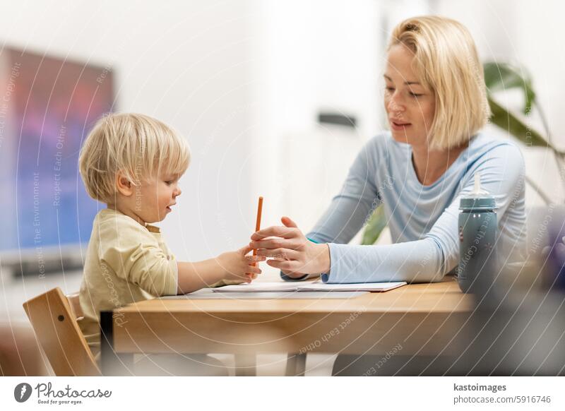 Caring junge kaukasische Mutter und kleinen Sohn Zeichnung Malerei in Notebook zu Hause zusammen. Liebevolle Mutter oder Kindermädchen mit Spaß am Lernen und Spielen mit ihrem kleinen 1,5 Jahre alten Säugling Baby Junge Kind.