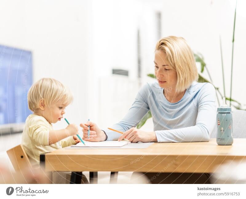 Caring junge kaukasische Mutter und kleinen Sohn Zeichnung Malerei in Notebook zu Hause zusammen. Liebevolle Mutter oder Kindermädchen mit Spaß am Lernen und Spielen mit ihrem kleinen 1,5 Jahre alten Säugling Baby Junge Kind.