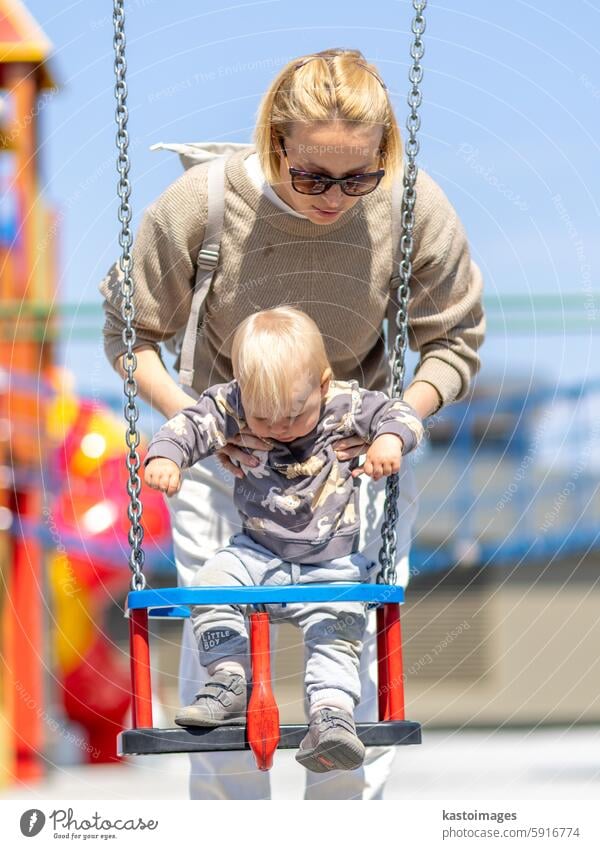 Mutter schiebt ihr Kleinkind auf einer Schaukel auf dem Spielplatz im Freien. Kind Glück Säugling Baby Junge Sohn Familie pendeln Frau Kinderspielplatz Kindheit