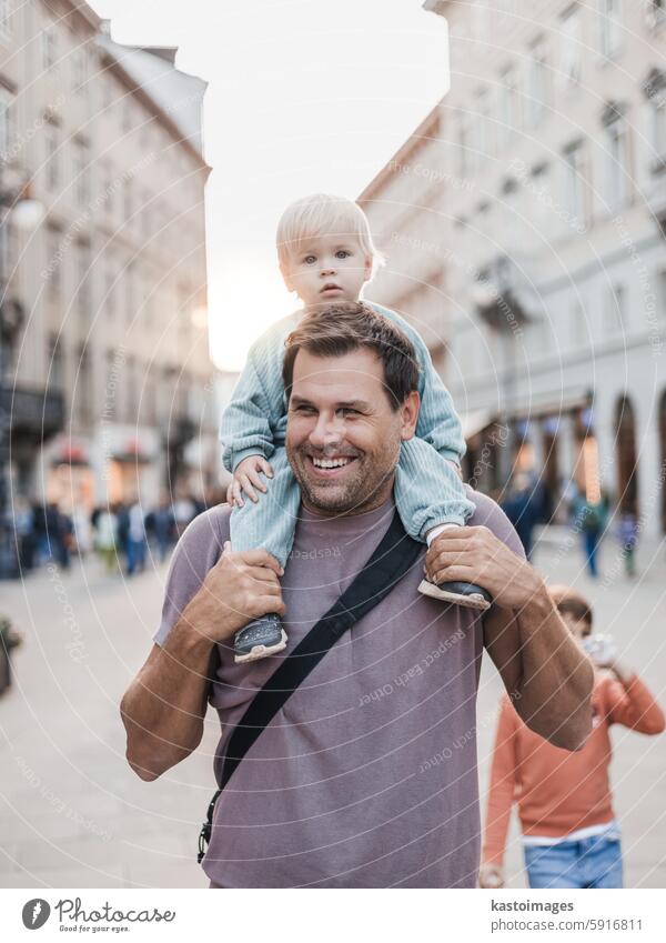 Porträt eines lächelnden Vaters, der sein Kleinkind auf einem Familienurlaub huckepack durch die Stadt trägt. Alles Gute zum Vatertag. Spaß Glück Sohn im Freien