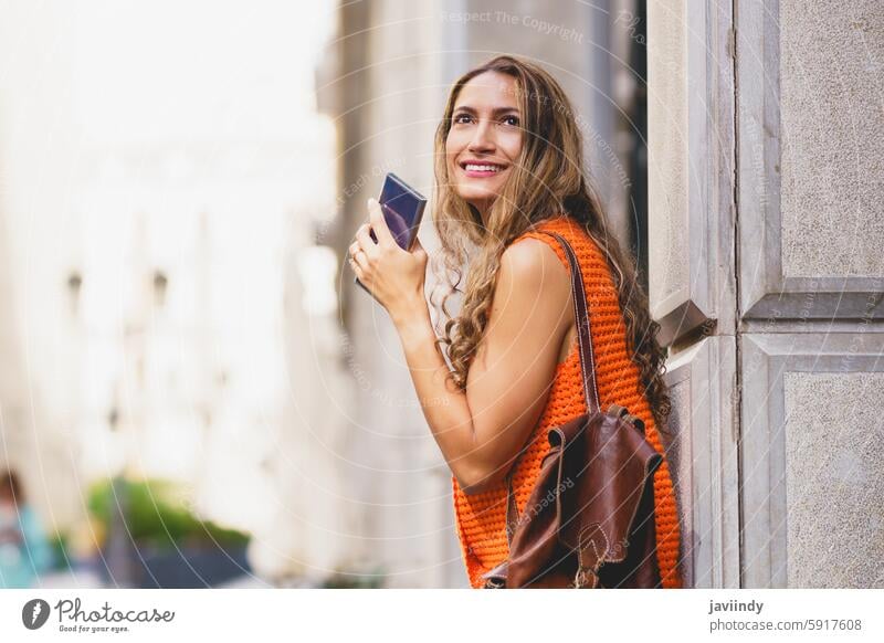 Frau mit Handy in der Hand und Blick nach oben beim Besuch einer Stadt Latein Schönheit Halt aufschauend besuchen Großstadt urban Straße im Freien Lifestyle