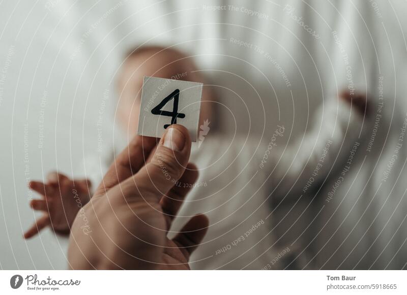 Würfel mit der Zahl 4 in der Hand, im Hintergrund verschwommen ein Baby Wachstum wachsen Jubiläum menschliche hand würfel zahlen Ziffern & Zahlen Glück Farbfoto