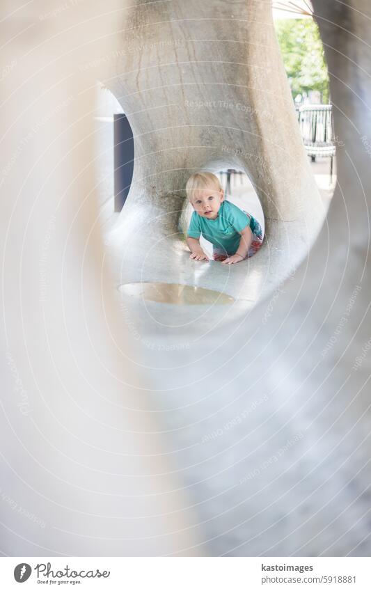 Kind spielt auf Spielplatz im Freien. Kleinkind spielt auf Schule oder Kindergarten Hof. Aktives Kind auf Stein gemeißelter Rutsche. Gesunde Sommeraktivität für Kinder. Kleiner Junge klettert im Freien.