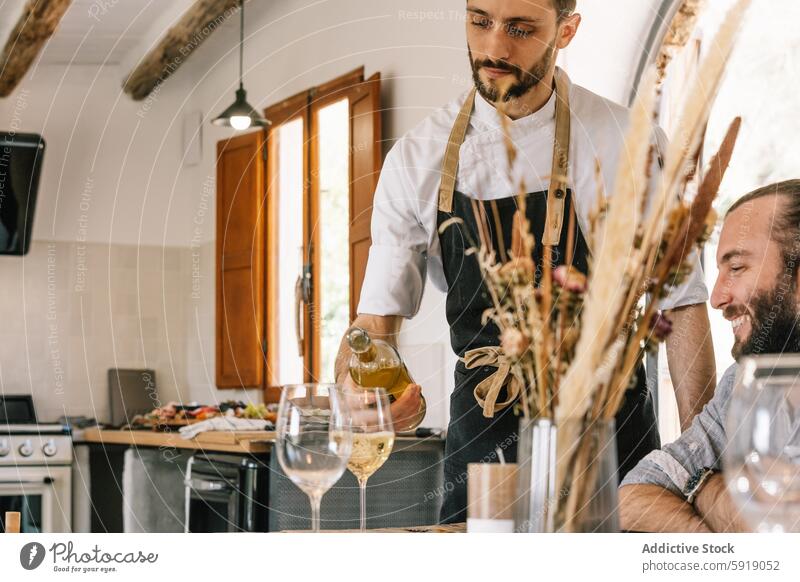 Privatkoch serviert Wein an einen Mann bei einem Küchentreffen Weißwein Servieren Lächeln Gast Gießen Abfertigungsschalter warm einladend rustikal Atmosphäre