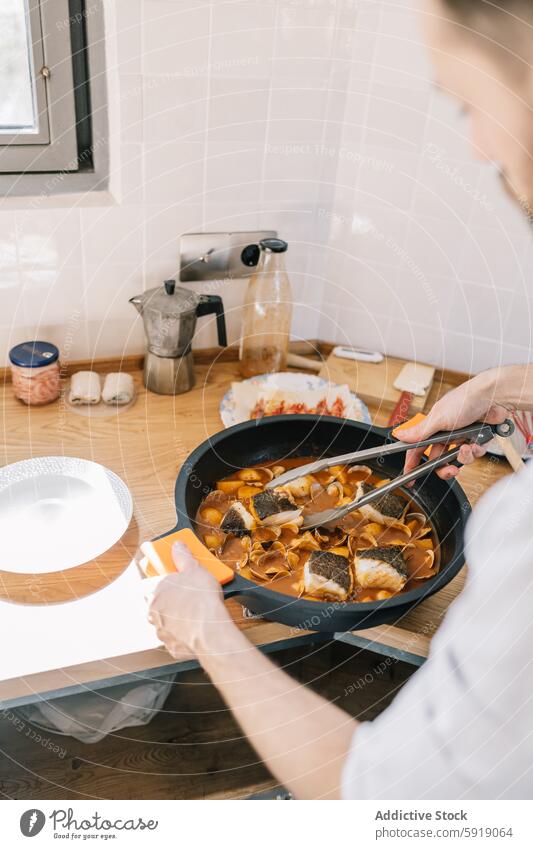 Privatkoch bei der Zubereitung eines Fischgerichts in einer gemütlichen Wohnküche Küchenchef Essen zubereiten Pfanne Mann vorbereitend Lebensmittel Speise