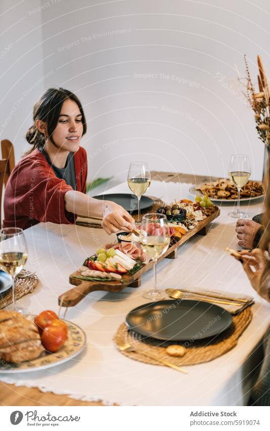 Frau serviert Essen bei gemütlicher Dinnerparty mit Freunden Servieren Lebensmittel Abendessen Party Wein Glas Charcuterie Holzplatte Tisch heimwärts lässig