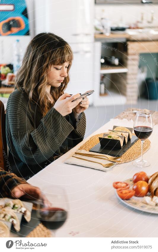 Junge Frau beim Telefonieren während einer Mahlzeit mit Freunden Smartphone speisend Tisch Gerichte Wein Glas Rotwein gemütlich heimwärts sozial Lebensmittel