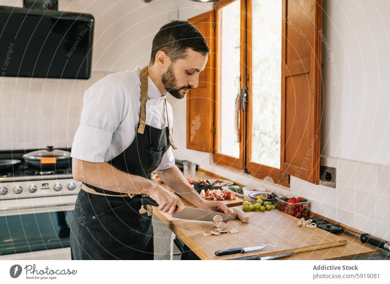 Privatkoch, der in der Küche Würstchen zubereitet und sich auf seine Aufgabe konzentriert Mann Essen zubereiten zerkleinernd Wurstwaren Zutaten Vorbereitung