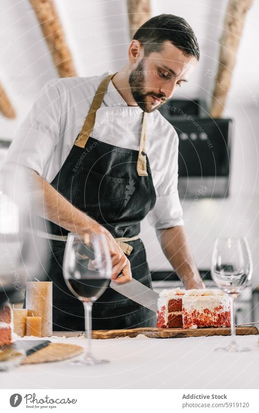 Privatkoch schneidet Kuchen in der Küche mit Konzentration und Präzision männlich Schneiden modern professionell weißes Hemd dunkle Schürze Fokus