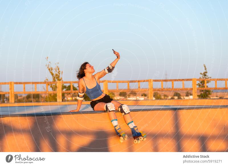 Junge Frau, die bei Sonnenuntergang Rollschuh fährt und ein Selfie macht Rollerskate Skateplatz Sportbekleidung Fangvorrichtung goldene Stunde Sommer im Freien