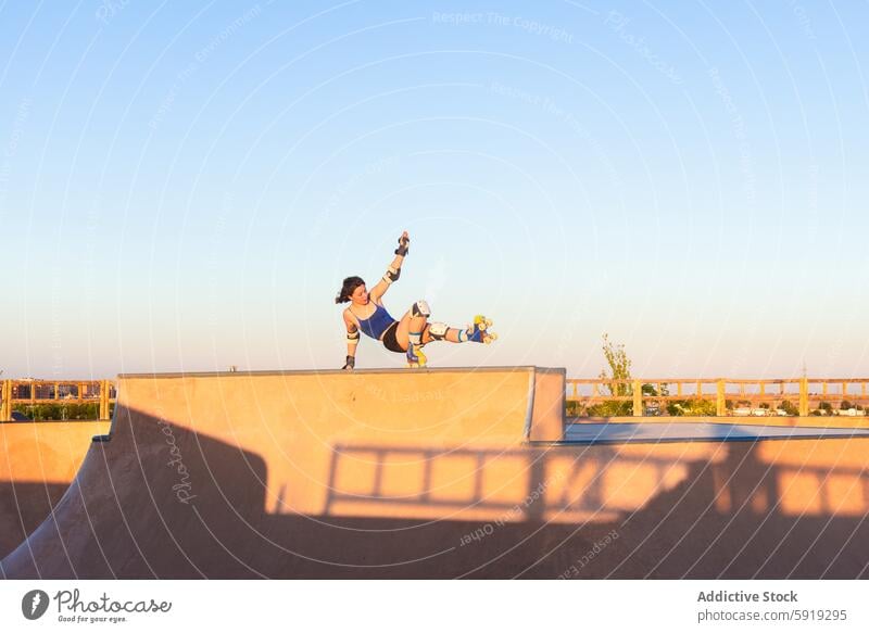 Junge Frau, die bei Sonnenuntergang einen Trick auf Rollschuhen vorführt Mädchen Rollerskate Skateplatz Stunt Sport Aktivität im Freien jung sportlich Leistung