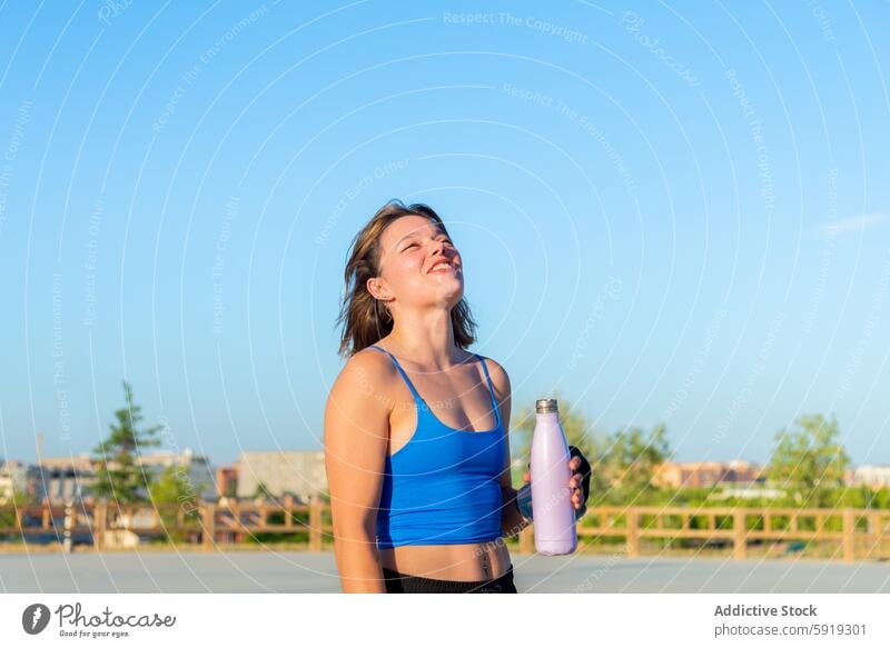 Junge Frau, die eine Pause in einem Skatepark genießt Skateplatz Rollschuhlaufen Wasserflasche sonnig Blauer Himmel Lächeln heiter jung im Freien Freizeit Sport