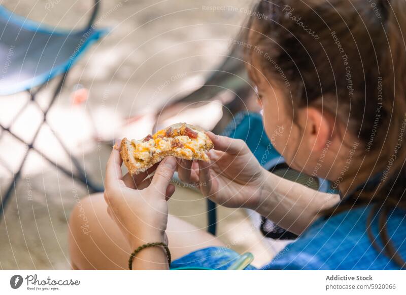 Junge unerkennbare Frau mit einem Stück Pizza in der Hand, die eine Mahlzeit am Lagerfeuer im Freien genießt Wohnmobil Essen am Lagerfeuer Natur Camping-Küche