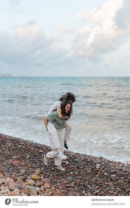 Lächelnde Frau, die ihren homosexuellen Geliebten huckepack am Strand trägt Freundin Huckepack lesbisch Spaß haben sorgenfrei Partnerschaft Liebe Umarmen Meer