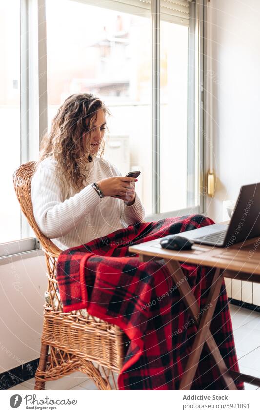 Junge Frau surft auf ihrem Smartphone, während sie mit ihrem Laptop am Tisch sitzt benutzend Mobile Browsen freiberuflich Arbeit zu Hause Surfen abgelegen