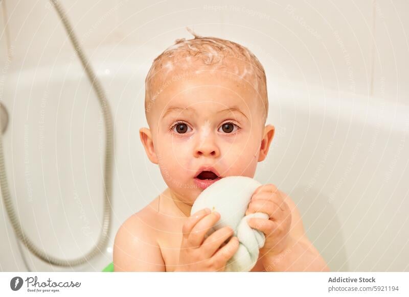 Ein Kind in der Badewanne mit einem Kopf voller Seife und einem nassen Handtuch in den Händen bezaubernd Baby Baden Körper Junge braun Schaumblase Pflege