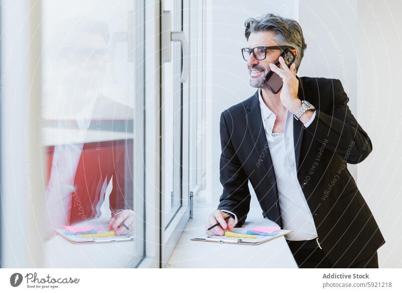 Eine elegante Führungskraft telefoniert, während sich im Fenster eine Stadtlandschaft spiegelt, die das vernetzte Geschäft symbolisiert. Exekutive Anruf Telefon