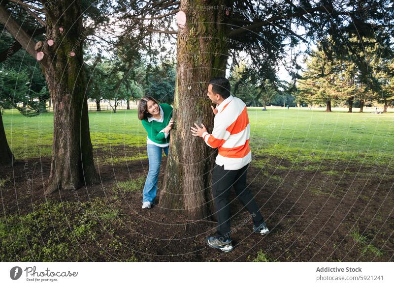 Junges lateinamerikanisches Paar genießt einen spielerischen Moment im Park lateinisches Paar jung Frau Mann guckend Baum durchsuchend üppig (Wuchs) Gras