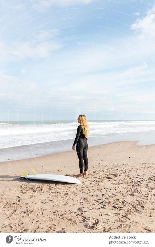 Junge Frau steht neben einem Surfbrett am Strand Küste Ufer Meeresufer Hobby Aktivität Zeitvertreib Sport heiter MEER Glück Wasser Gezeiten winken Lächeln