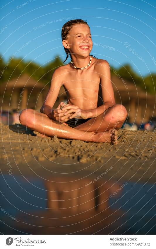 Hemdloser Junge schaut am Strand weg Wegsehen Lächeln sitzen Sand Urlaub Sommer nass ohne Hemd Panzer Halskette Beine gekreuzt Lifestyle Wasser Glück Kind