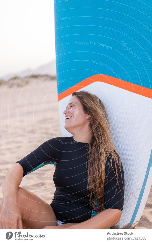 Glücklicher Surfer mit Paddleboard am Strand Frau Paddelbrett Zusatzplatine SUP Meeresufer Seeküste Sommer Lächeln Surfbrett heiter sitzen froh Ufer Holzplatte