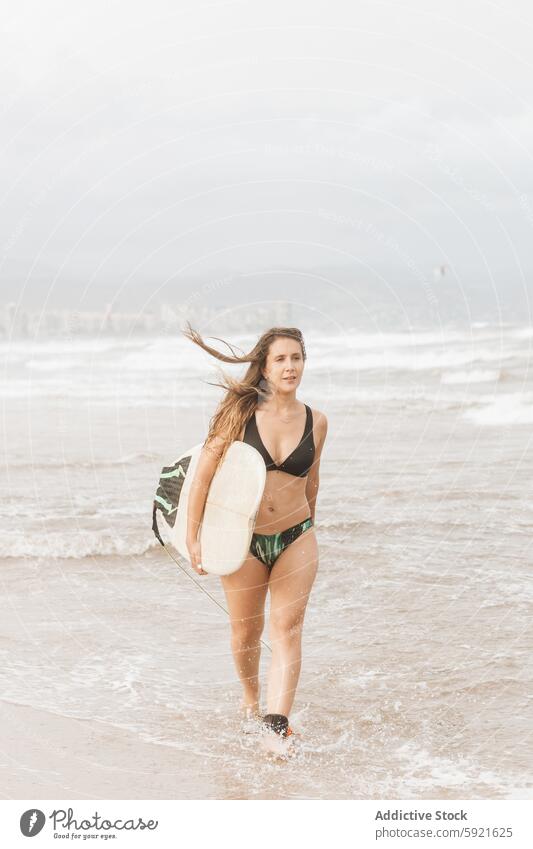 Surfer mit Surfbrett am Strand fliegendes Haar Sport Körper laufen Badebekleidung Surfen genießen Frau Meeresufer Himmel Badeanzug Küste stürmisch nachdenken