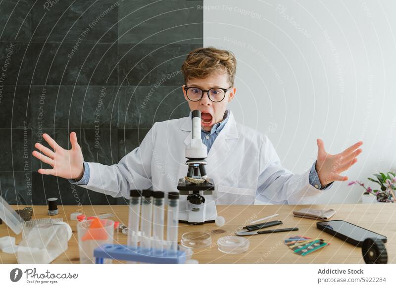 Überrascht Junge sitzt am Tisch mit Mikroskop und Reagenzgläsern in der Schule Schüler Überraschung Labor Chemie Wissenschaftler Flasche Experiment forschen