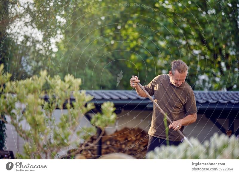 Ein geschickter Handwerker bei einer praktischen Arbeit im Freien, der einen Gartenbereich sorgfältig harkt und pflegt Kunsthandwerker Handarbeit Außenarbeit