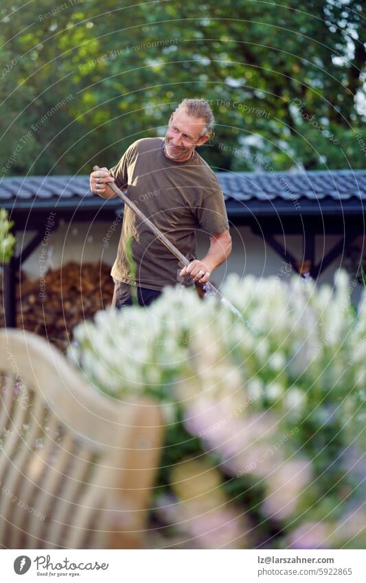 Ein geschickter Handwerker bei einer praktischen Arbeit im Freien, der einen Gartenbereich sorgfältig harkt und pflegt Kunsthandwerker Handarbeit Außenarbeit