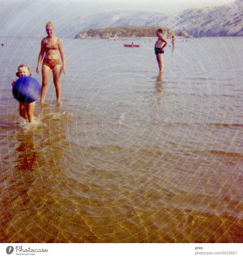 Urlaub am Meer in den frühen 70er Jahren | Frau mit Bikini läuft hinter einem kleinen Mädchen mit Wasserball in den Händen durch das niedrige Wasser Adria