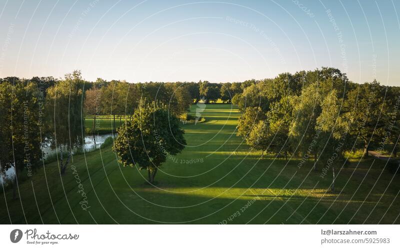 Eine ruhige Luftaufnahme eines üppigen Golfplatzes, der in das warme Licht des Sonnenuntergangs getaucht ist. Ideal für Themen wie Entspannung, Natur und Sport. Dieses Bild fängt die friedliche Schönheit des Golfspiels ein.