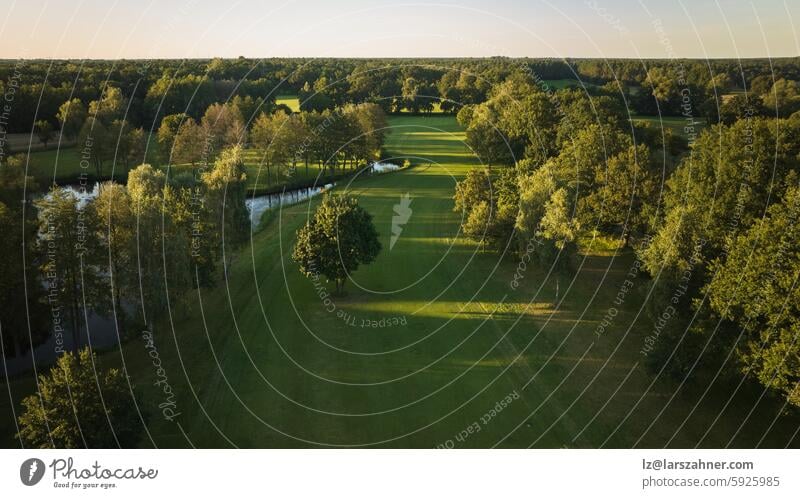 Eine ruhige Luftaufnahme eines üppigen Golfplatzes, der in das warme Licht des Sonnenuntergangs getaucht ist. Ideal für Themen wie Entspannung, Natur und Sport. Dieses Bild fängt die friedliche Schönheit des Golfspiels ein.