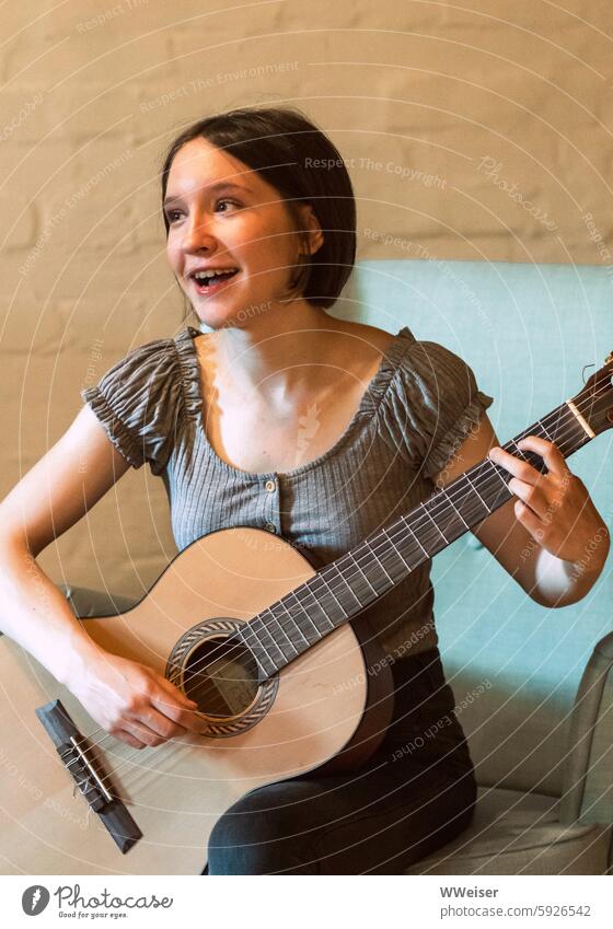 Ein junges Mädchen singt fröhlich und inspiriert und spielt Gitarre junge Frau singen spielen Musik musizieren Gesang sitzen Lied glücklich warm