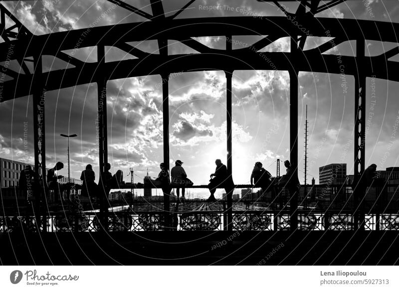 Silhouetten von jungen Leuten, die im Sonnenuntergang auf der Stahlbrücke sitzen voller Rahmen Hacker Brücke antik Architektur Hintergründe schwarz-weiß Gebäude