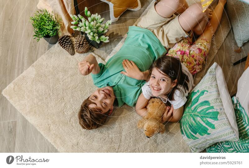 Lachende und sich entspannende Kinder auf einem Teppich in einem gemütlichen Zelt zu Hause, umgeben von Kissen und Pflanzen Glück Lügen Vorleger aussruhen