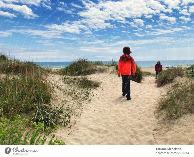 Junge mit orangem Pulli läuft auf Sand in den Dünen Richtung Meer Kind Sandstrand Himmel Ferien & Urlaub & Reisen Küste Erholung Tourismus Mittelmeer Wolken